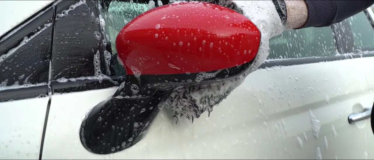 Still from the official Innovacar video: foam wash of an Abarth 595, the red mirror covered in water